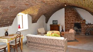 Una habitación rústica con techo abovedado, chimenea y zona de comedor con mesa y sillas.