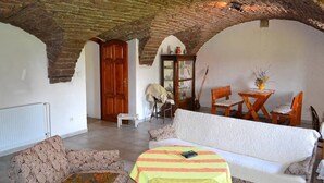 Un salón acogedor con un techo alto abovedado, un sofá blanco, sillones estampados y una mesita con mantel a rayas.
