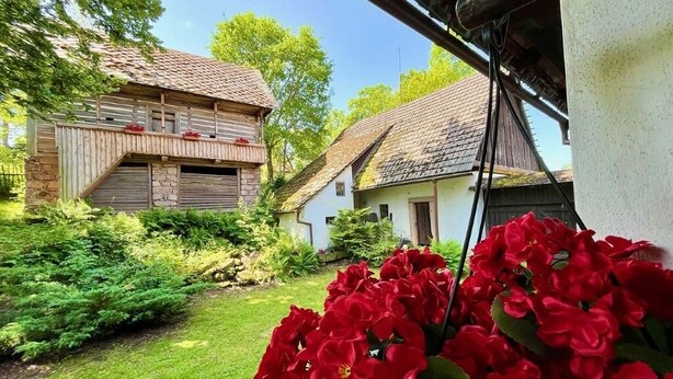 Un edificio rústico con base de piedra y estructura de madera, rodeado de un jardín cuidado con flores rojas.