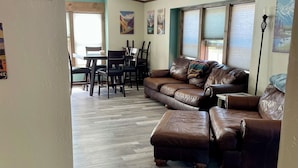 A living room with a sectional sofa, a dining table with chairs, and a herringbone-patterned wooden floor. - Livingston MT Paradise Unit B (Livingston)