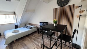 A small, modern room with a bed, a desk, and a chair. There is a clock on the wall and a window providing natural light. - Cosy furnished studio in a quiet location near the Cathedral (Orléans)