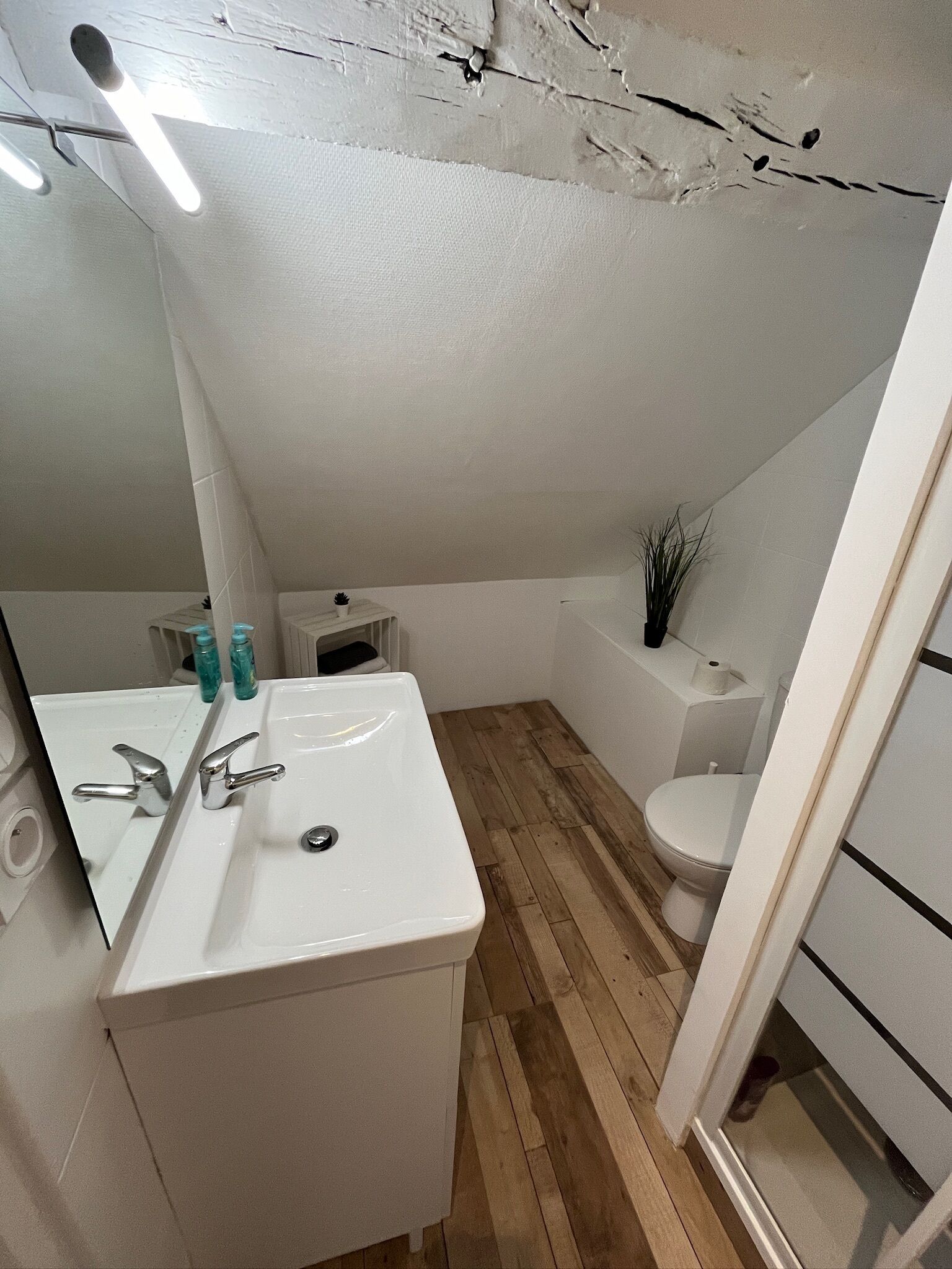 Een badkamer met een witte wastafel, twee kraanwerk, een spiegel, een toilet en een klein plankje met toiletartikelen.