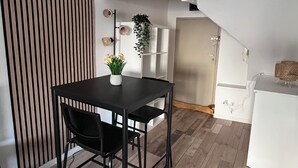 A dining area with a black table and chairs, a clock on the wall, and a staircase leading to an upper level. - Cosy furnished studio in a quiet location near the Cathedral (Orléans)