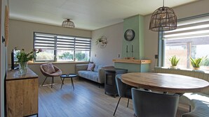 Un salon moderne comprenant un canapé, des fauteuils, une table ronde, une cheminée et de grandes fenêtres équipées de stores.