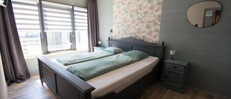 A bedroom with a bed, a nightstand, a mirror, and a window with curtains.