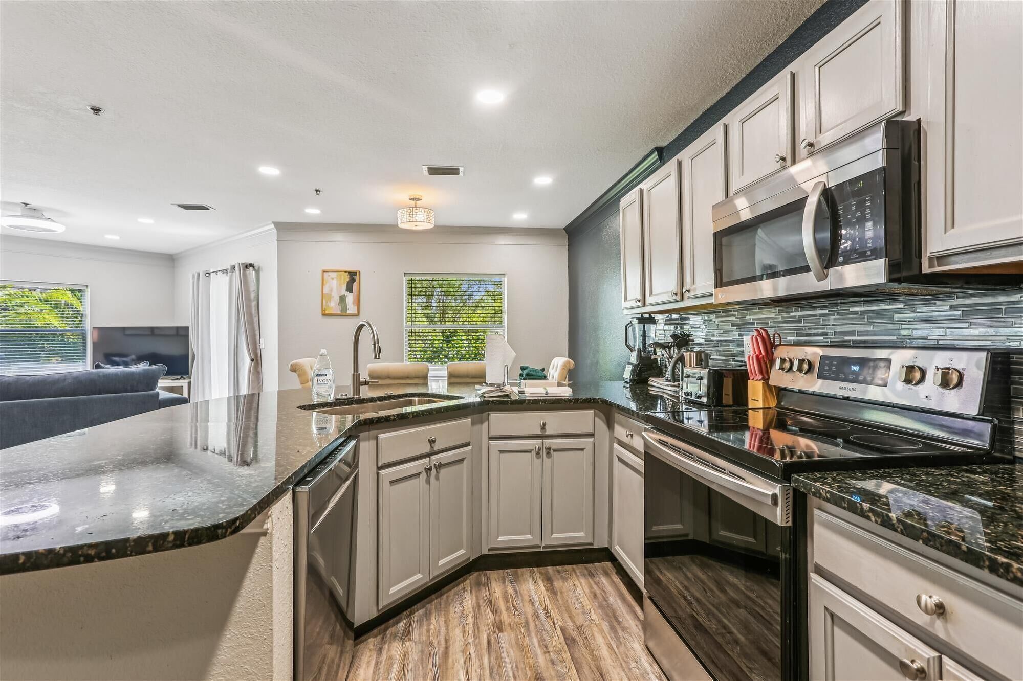 A modern kitchen with white cabinetry, a large island, stainless steel appliances, and a view of the outdoors.