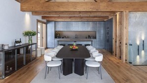 A modern kitchen with a long dining table, white chairs, and a wooden ceiling.