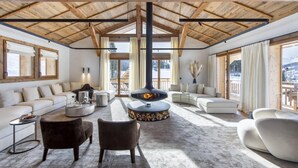 A spacious living room with a high wooden ceiling, a fireplace, and large windows offering a view of the outdoors.