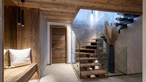 A modern interior with a wooden staircase, a bench, and a glass door leading to another room.