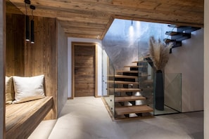 Um interior moderno com escada de madeira, um banco e uma porta de vidro que dá para outro cômodo.