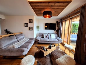 Un salon moderne avec un canapé gris, une table basse en bois et une grande fenêtre donnant sur un paysage verdoyant.