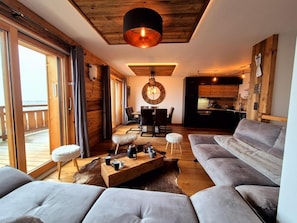 Un vaste espace de vie agrémenté d’un grand canapé gris, d’une table basse en bois avec des tasses, et d’une décoration rustique comprenant un tapis en fourrure et un plafond en bois.
