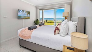 Un dormitorio con cama, ventilador de techo, televisor, lámpara y vista al océano.