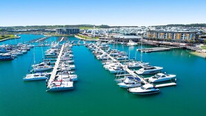 Un puerto deportivo con numerosos barcos amarrados, un moderno complejo de edificios y un cielo azul despejado.