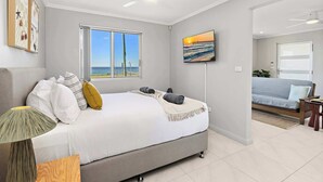 Ein Schlafzimmer mit einem Bett, einem Deckenventilator, einem Fernseher und einem Fenster mit Meerblick.