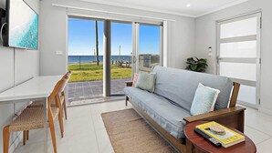 Ein modernes Wohnzimmer mit einer Couch, einem Esstisch mit Stühlen, einem an der Wand montierten Fernseher und Meerblick durch große Schiebetüren.