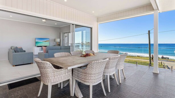 A dining area with a view of the ocean, a sofa, and a TV. - Seabreeze on the Beach "Feng" (Warilla)