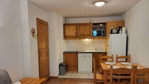 Una cocina compacta con armarios de madera, un microondas, un refrigerador y una mesa de comedor con sillas.