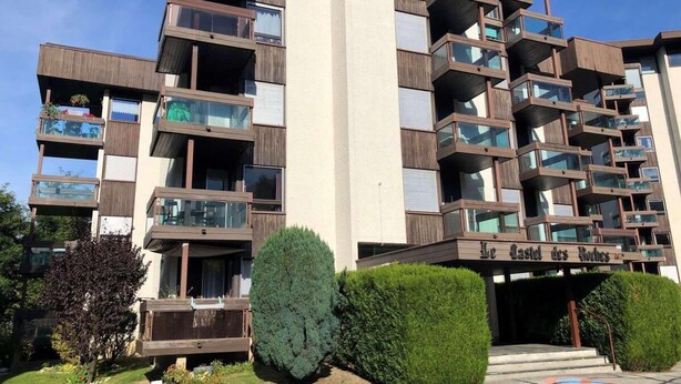 A multi-story residential building with balconies, a central entrance, and a sign reading "Le Castel des Roches."