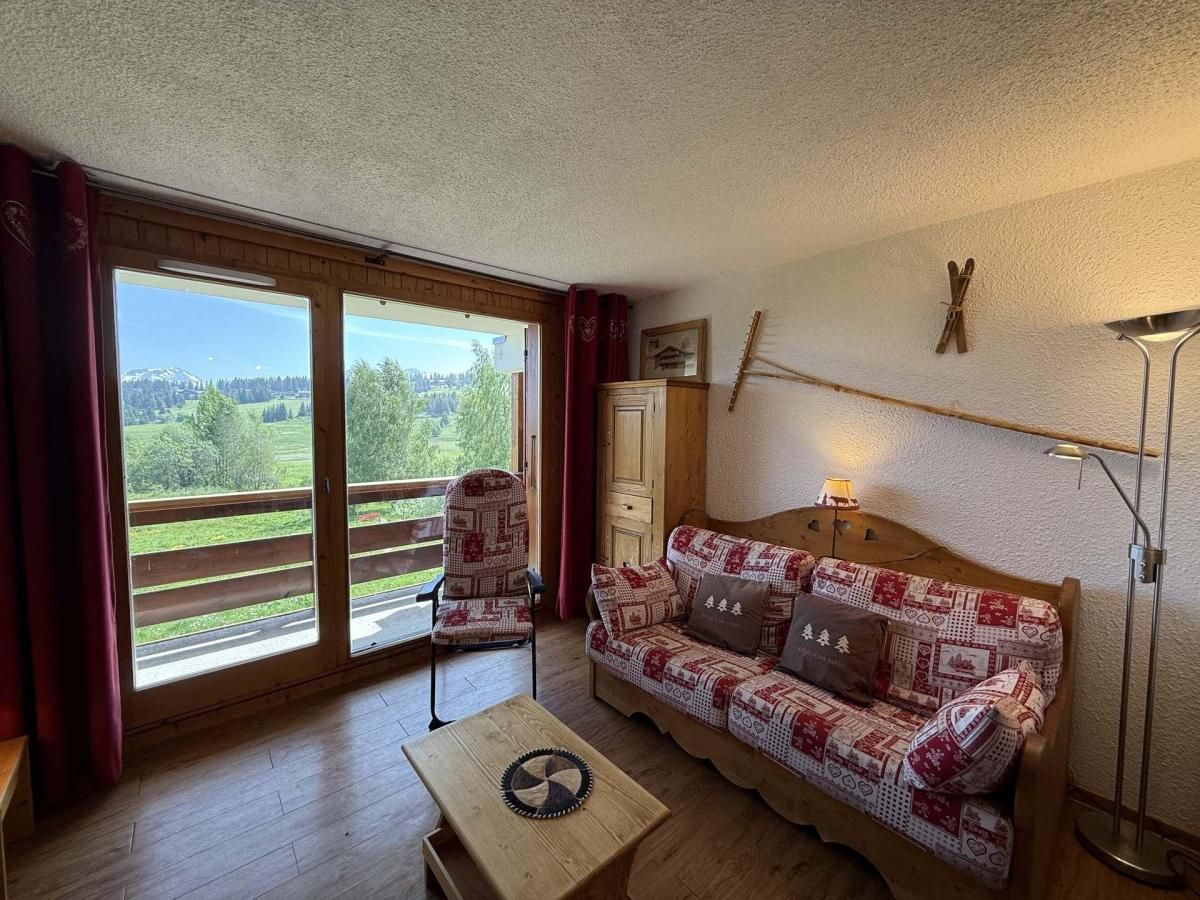 A cozy room with a patterned sofa, a wooden table, and a view through large sliding glass doors to a balcony.