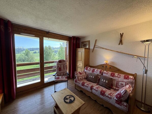 A cozy room with a patterned sofa, a wooden table, and a view through large sliding glass doors to a balcony.