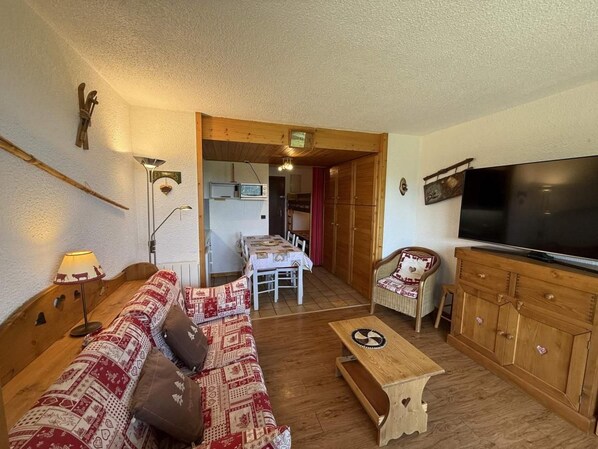 A cozy living room with a sofa, a wooden cabinet, a television, and a dining area with a table and chairs.