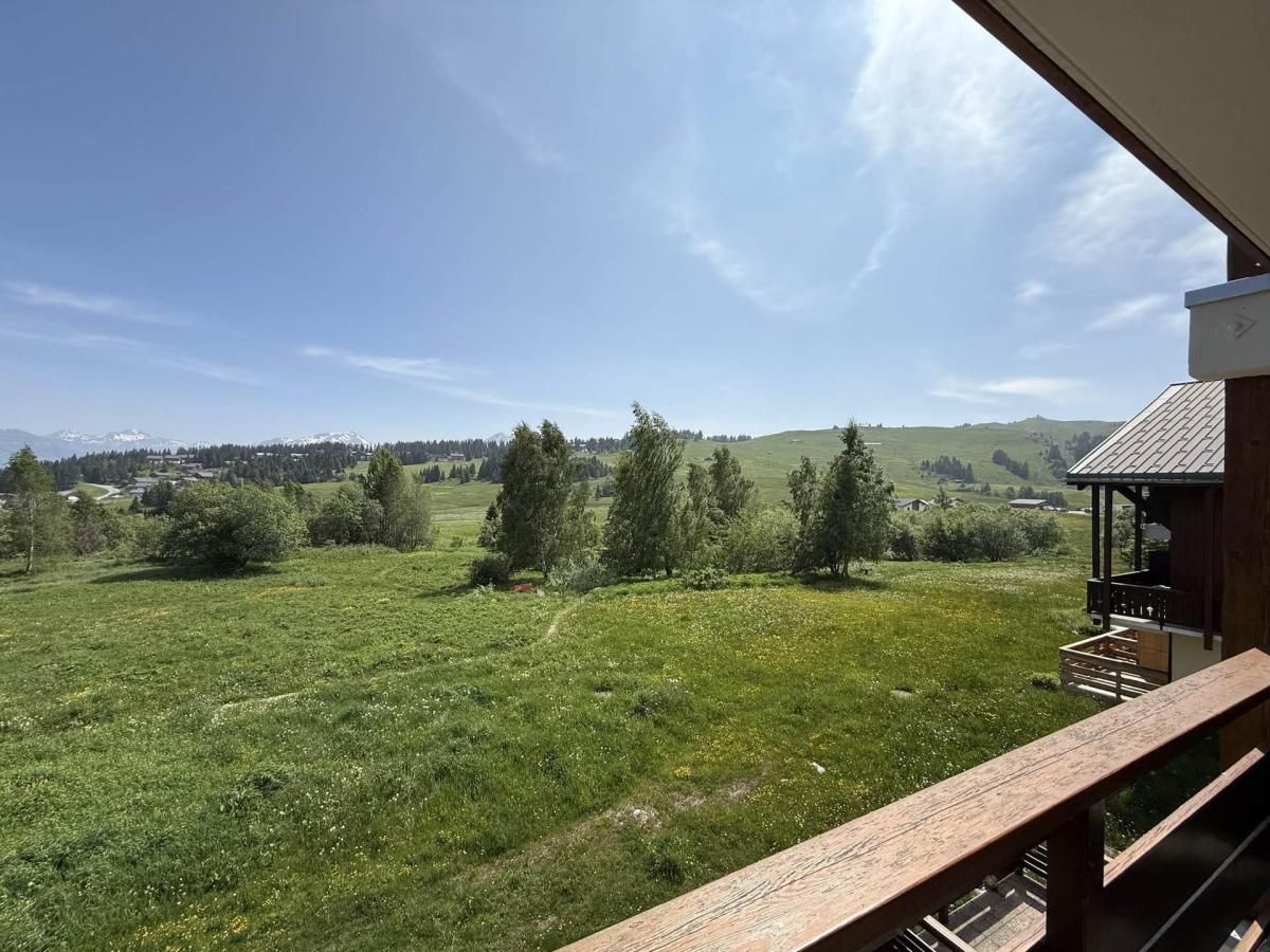 A balcony with a view of a grassy field and trees, a wooden deck, and a small building with a sloped roof.