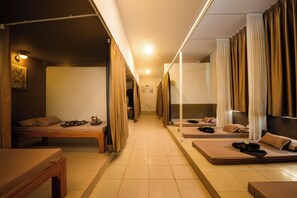 A corridor with multiple beds arranged on either side, each with a pillow and a small table.