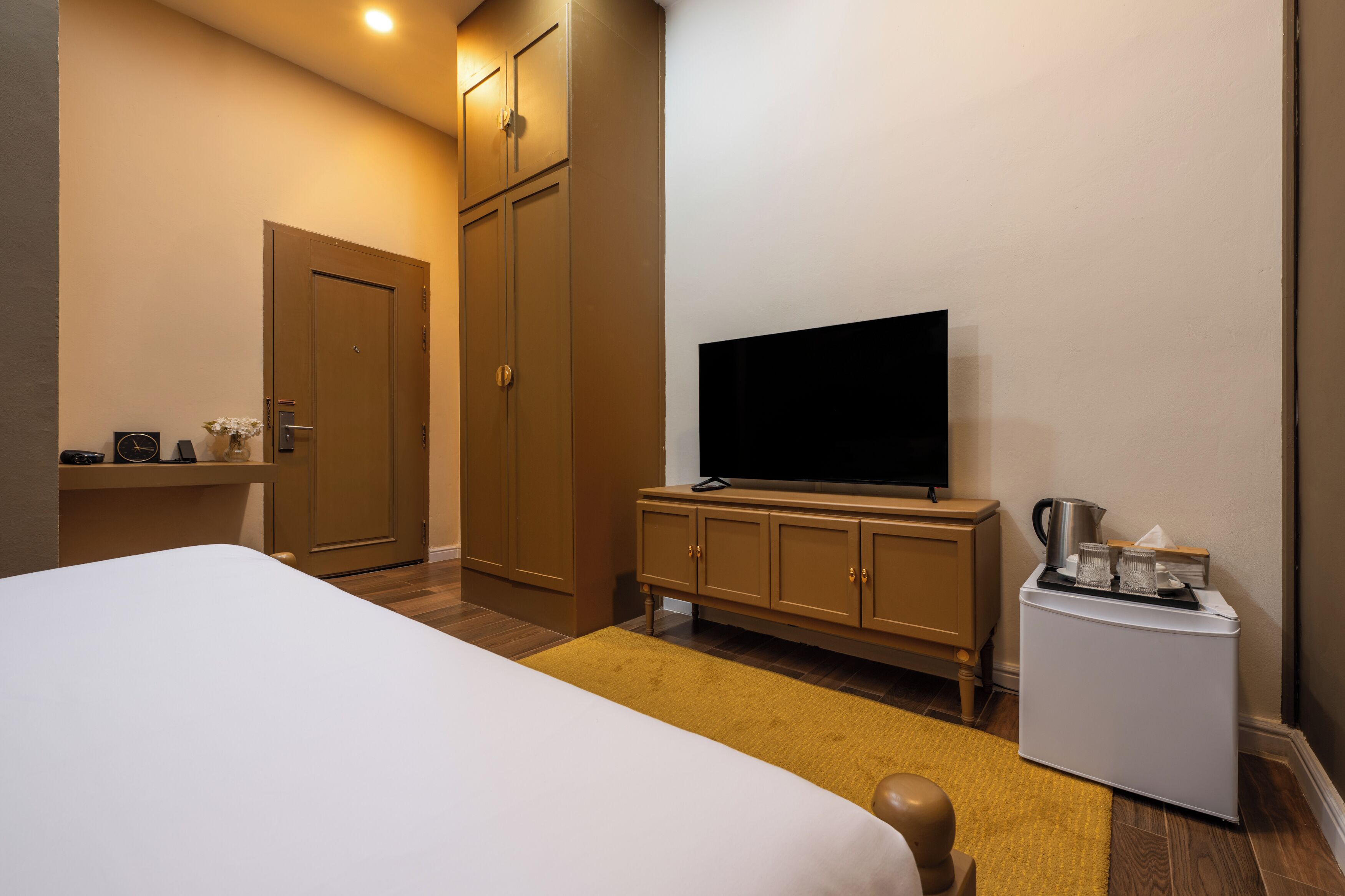 A hotel room with a bed, a television, a minibar, and a wardrobe.