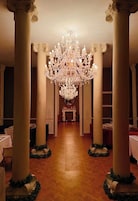 Un salón imponente con columnas ornamentales, un gran candelabro y mesas dispuestas para el servicio de comidas.