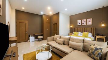 A modern hotel room with a sofa, a bed with yellow and white bedding, a small table with a vase of flowers, and a television on a desk.