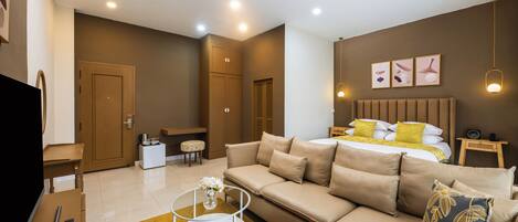 A modern hotel room with a sofa, a bed with yellow and white bedding, a small table with a vase of flowers, and a television on a desk.