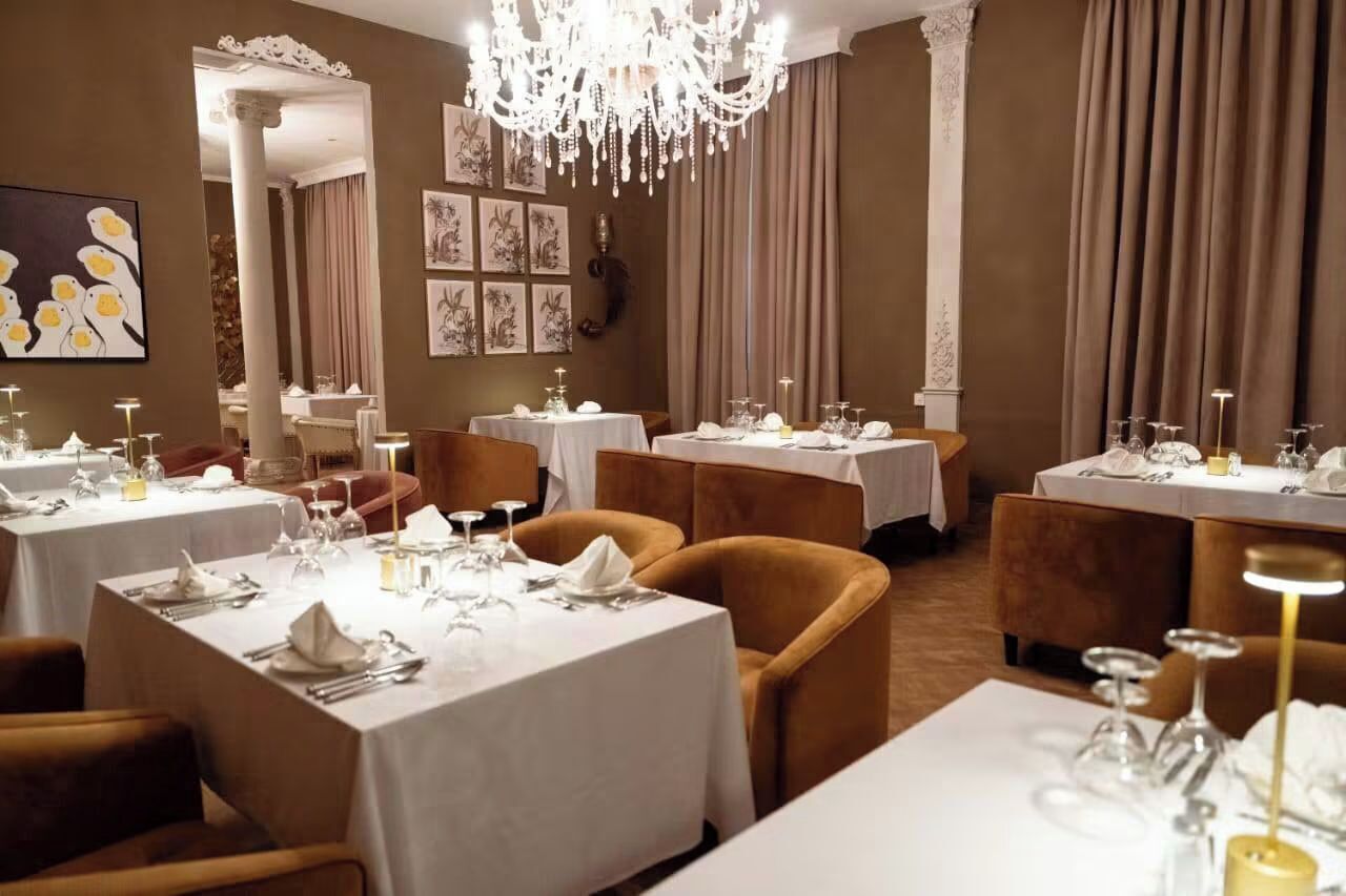 Un restaurante con varias mesas dispuestas para comer, con manteles blancos y candelabros dorados.