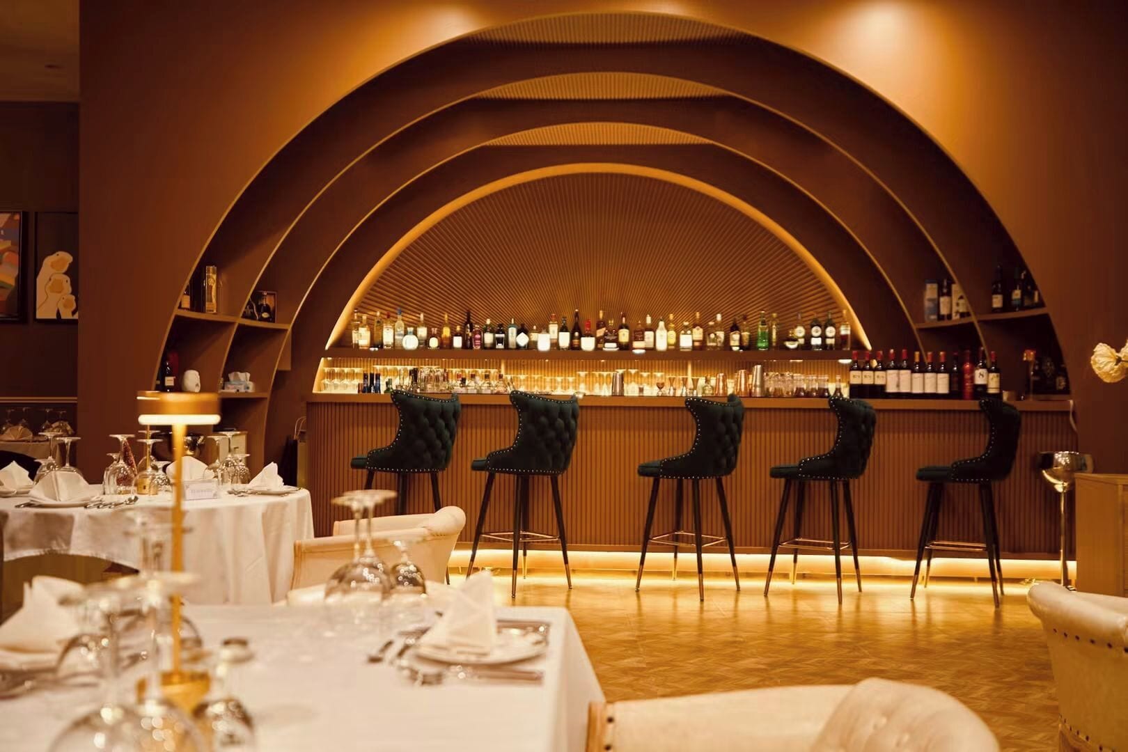 Een bar met een gebogen plafond, barstoelen en een goed gevulde drankenkast.