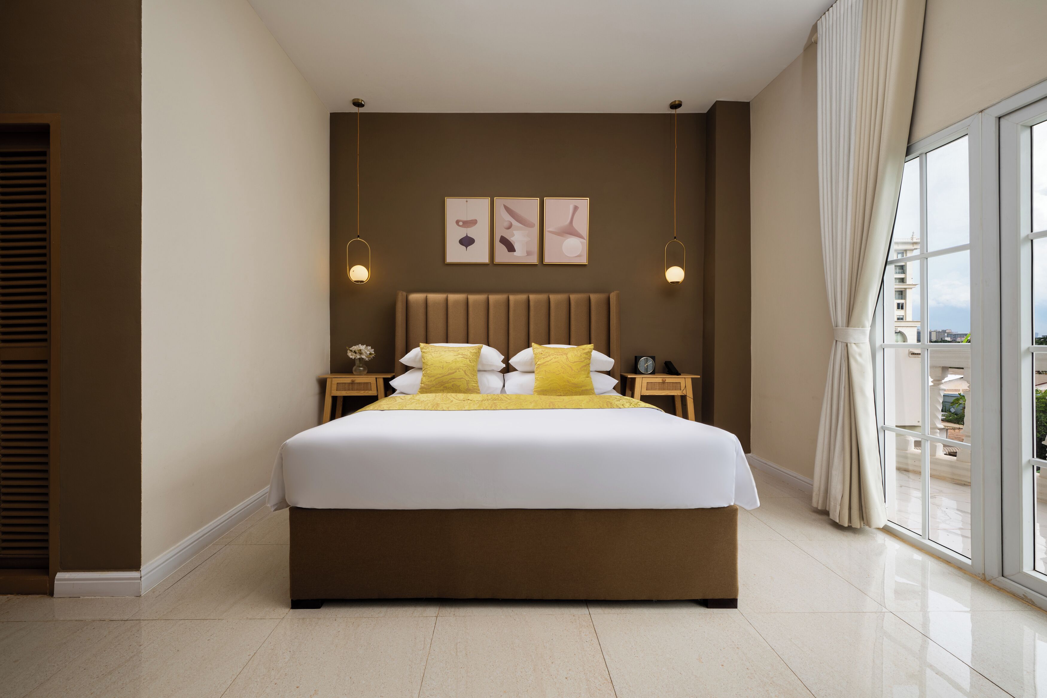 Une chambre d’hôtel moderne dotée d’un grand lit, d’une tête de lit, de tables de chevet et offrant une vue sur la ville grâce à de grandes fenêtres.