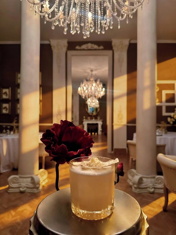 A luxurious interior with a chandelier, a glass of a creamy beverage, and a red rose on a table.