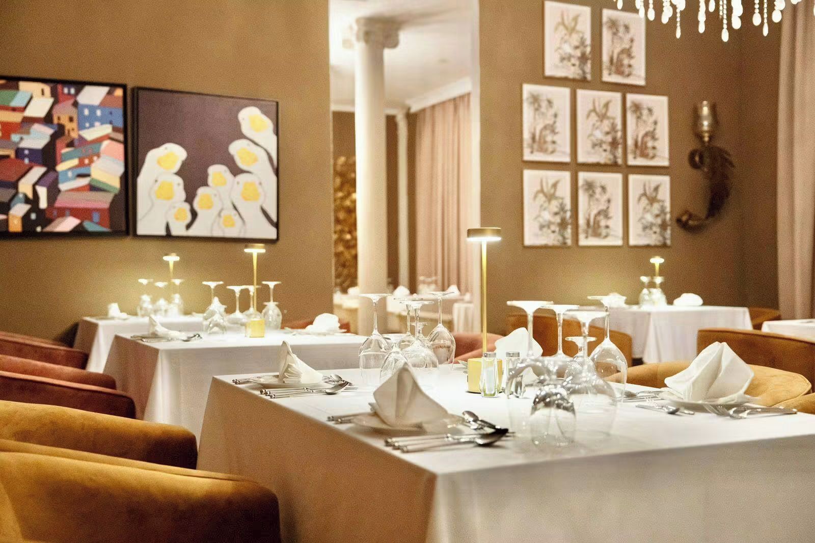 A dining area with tables set for service, framed artwork on the walls, and a chandelier.