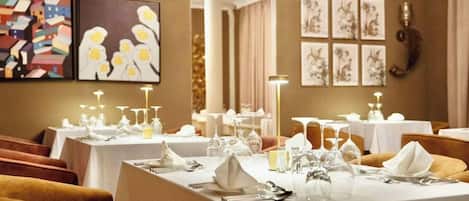 A dining area with tables set for service, framed artwork on the walls, and a chandelier.