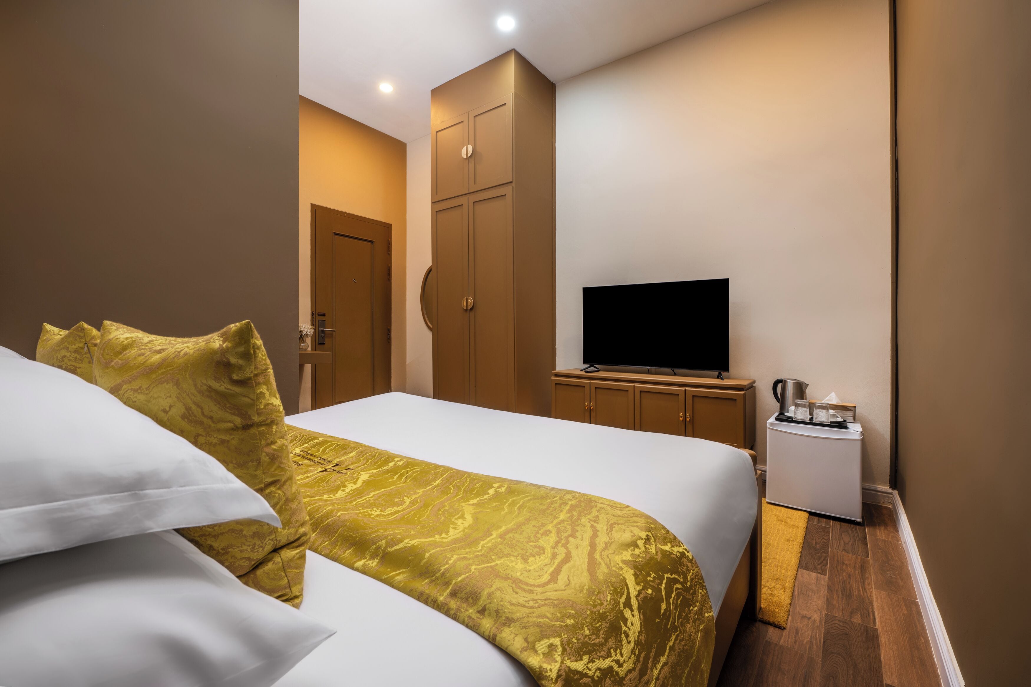 A hotel room with a bed, a television, a minibar, and a wardrobe.