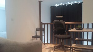 A small, furnished room with a wooden floor, a grey armchair, a black office chair, a small table with a plant, and a window with curtains. - Le Duplex d'Abi, quiet, overlooking courtyard, close to the center of Saint Étienne (Saint-Étienne)