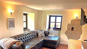 A living room with a leather sofa, a stone wall, and a wooden floor. - Wonderful property in a fantastic location. Family-friendly. Il Roseto I (Somano)