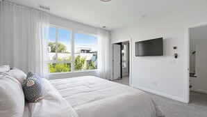 Ein modernes Schlafzimmer mit einem großen Bett, einem an der Wand montierten Fernseher und Blick ins Grüne.
