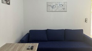 A room with a dark blue sofa, a wooden table with a remote control, and a wall-mounted picture. - Charming T1 bis apartment in Collobrières (Collobrières)