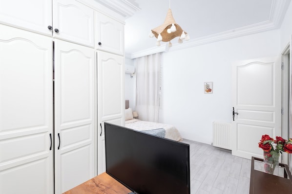 A bedroom with a bed, a TV, white wardrobes, a hanging light fixture, and a radiator.