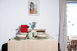 Ein Essbereich mit einem Tisch für vier Personen, einem roten Gerät und einer Vase mit getrockneten Blumen.