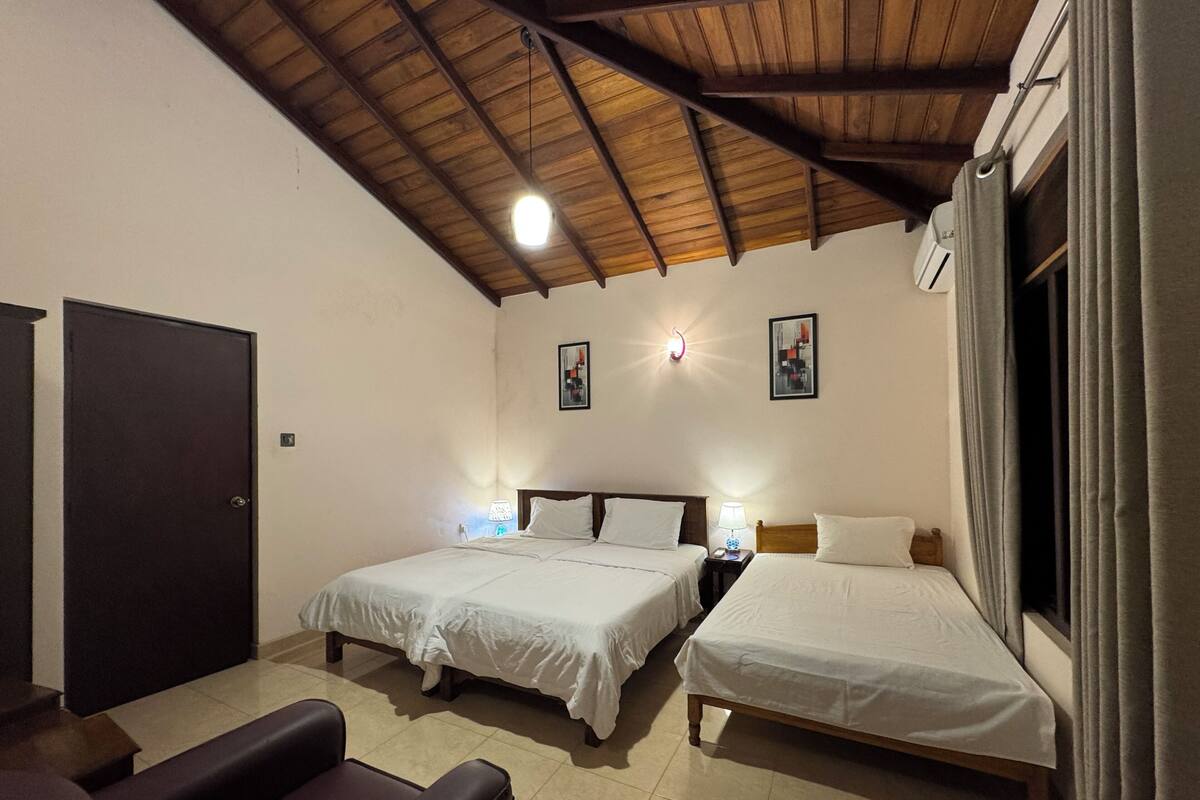 A hotel room with two beds, a wooden ceiling, a door, and a window with curtains.