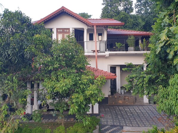A two-story house with a balcony, surrounded by lush greenery.
