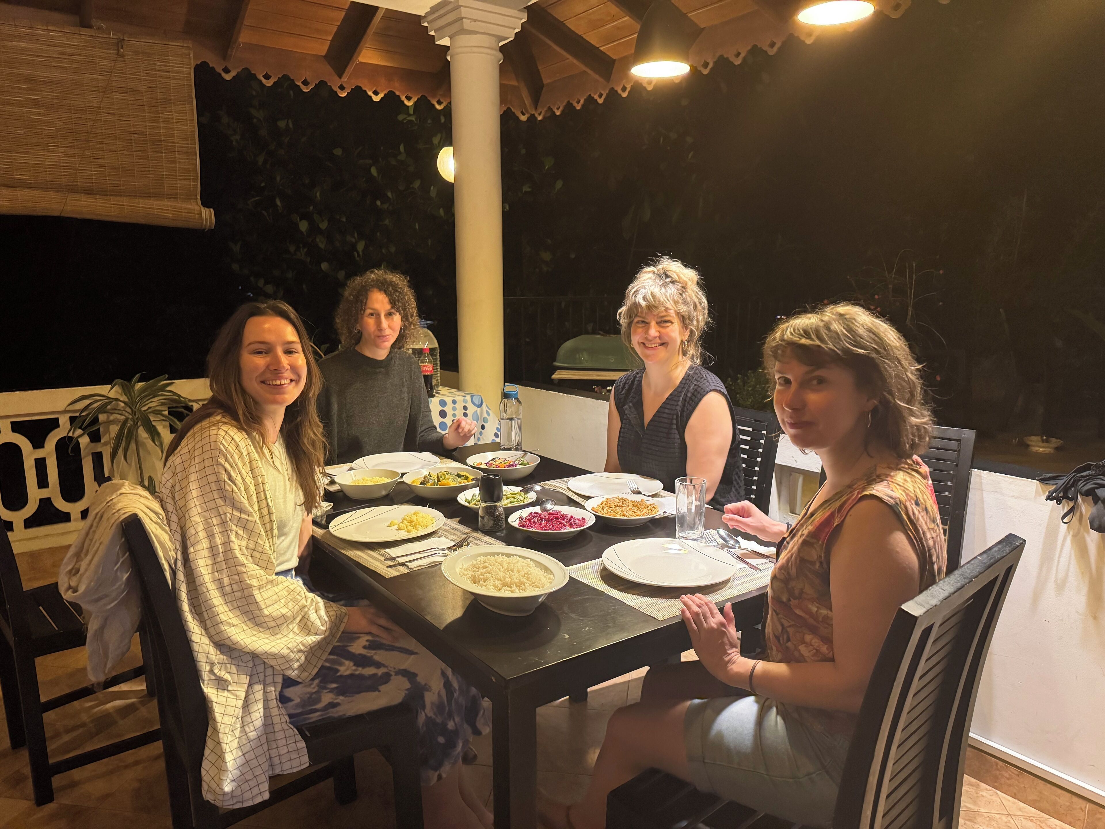 A group of people dining at an outdoor table with various dishes, a grill, and a bottle of water.