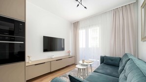 Ein modernes Wohnzimmer mit einer Couch, einem Flachbildfernseher, einem kleinen Tisch und einer Küchenzeile mit Backofen.