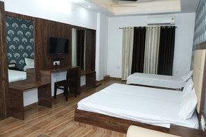 A hotel room with a wooden desk, a bed, a TV, and an air conditioning unit. - Amrit resort (Alwar)